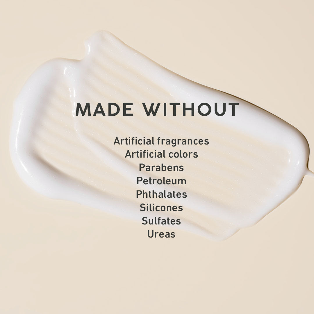 A cream-colored product smear on a warm beige background with the text 'MADE WITHOUT' and a list of excluded ingredients including artificial fragrances, parabens, petroleum, silicones, sulfates, and ureas.