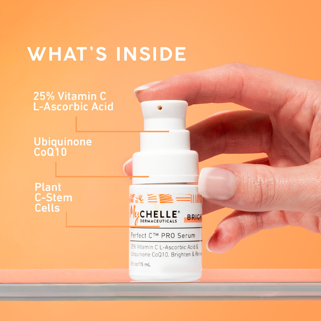 Hand holding a bottle of MyChelle Dermaceuticals Vitamin C serum with an orange background and text detailing ingredients.